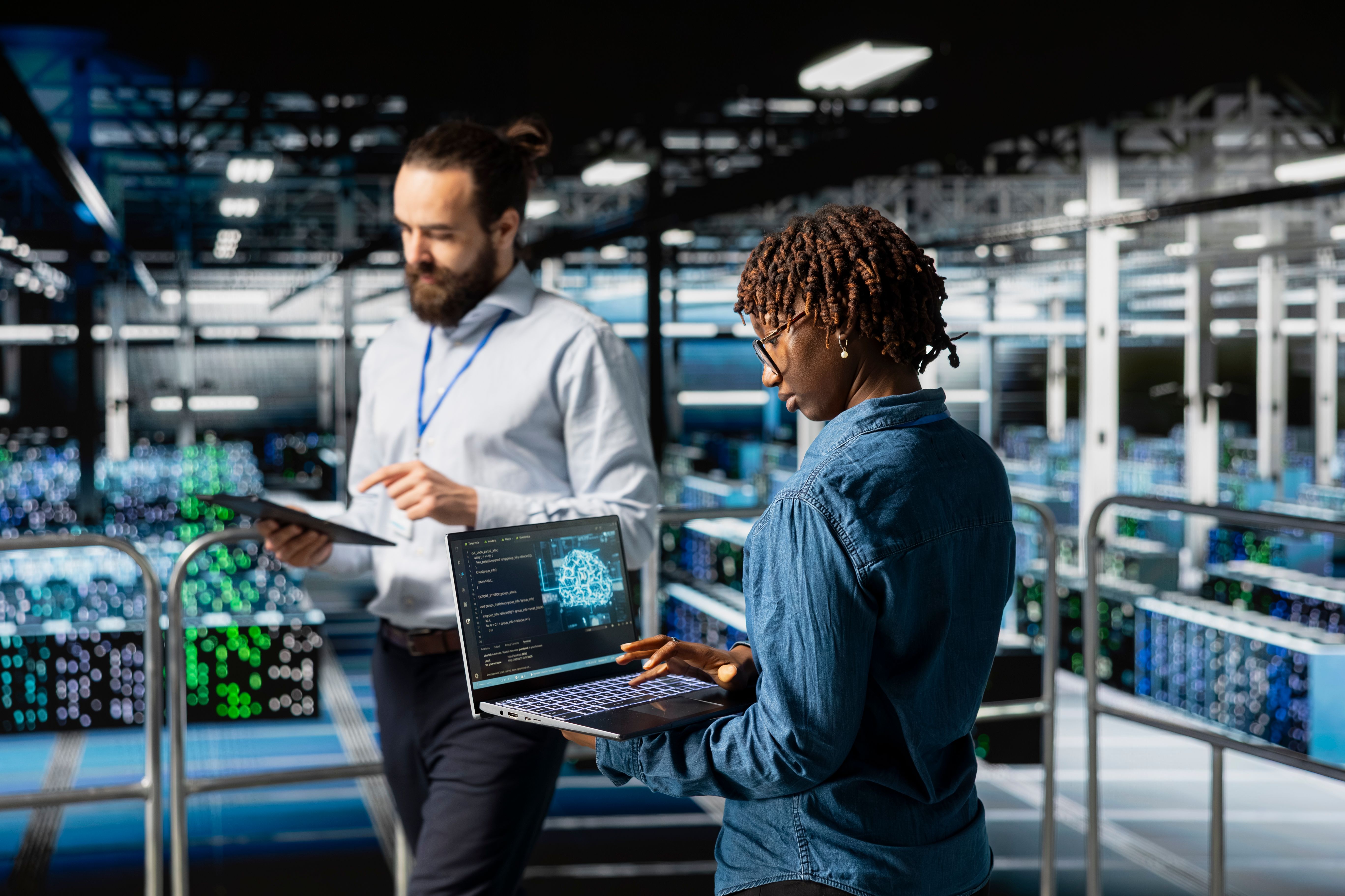 Two engineers working on a laptop and tablet in a data center